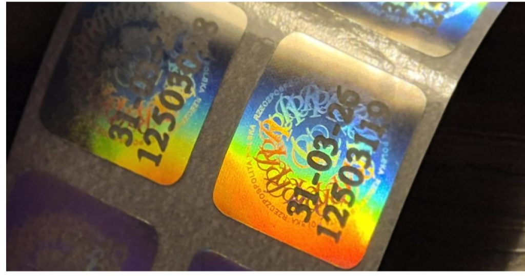 Zbliżenie naklejki 31-03-26 – efekt holograficzny i numer seryjny | kolekcjonerskie-hologramy.pl Pasek holograficznych naklejek 31-03-26 w różnych odcieniach, widoczne numery seryjne
